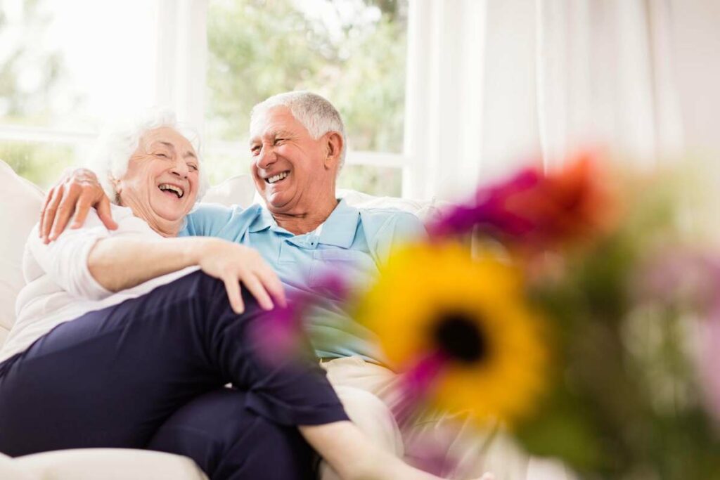 ER Senior Management | Senior couple on couch, laughing with flowers next to them